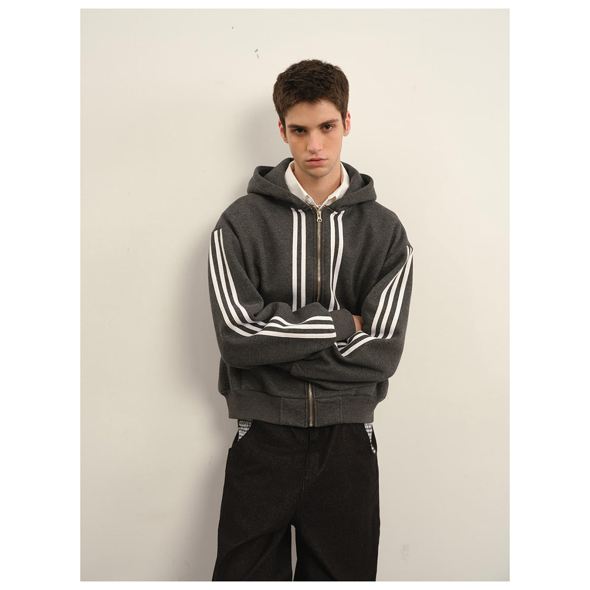 Front view of a person wearing a dark charcoal zip-up hoodie with white stripes on the sleeves and chest.