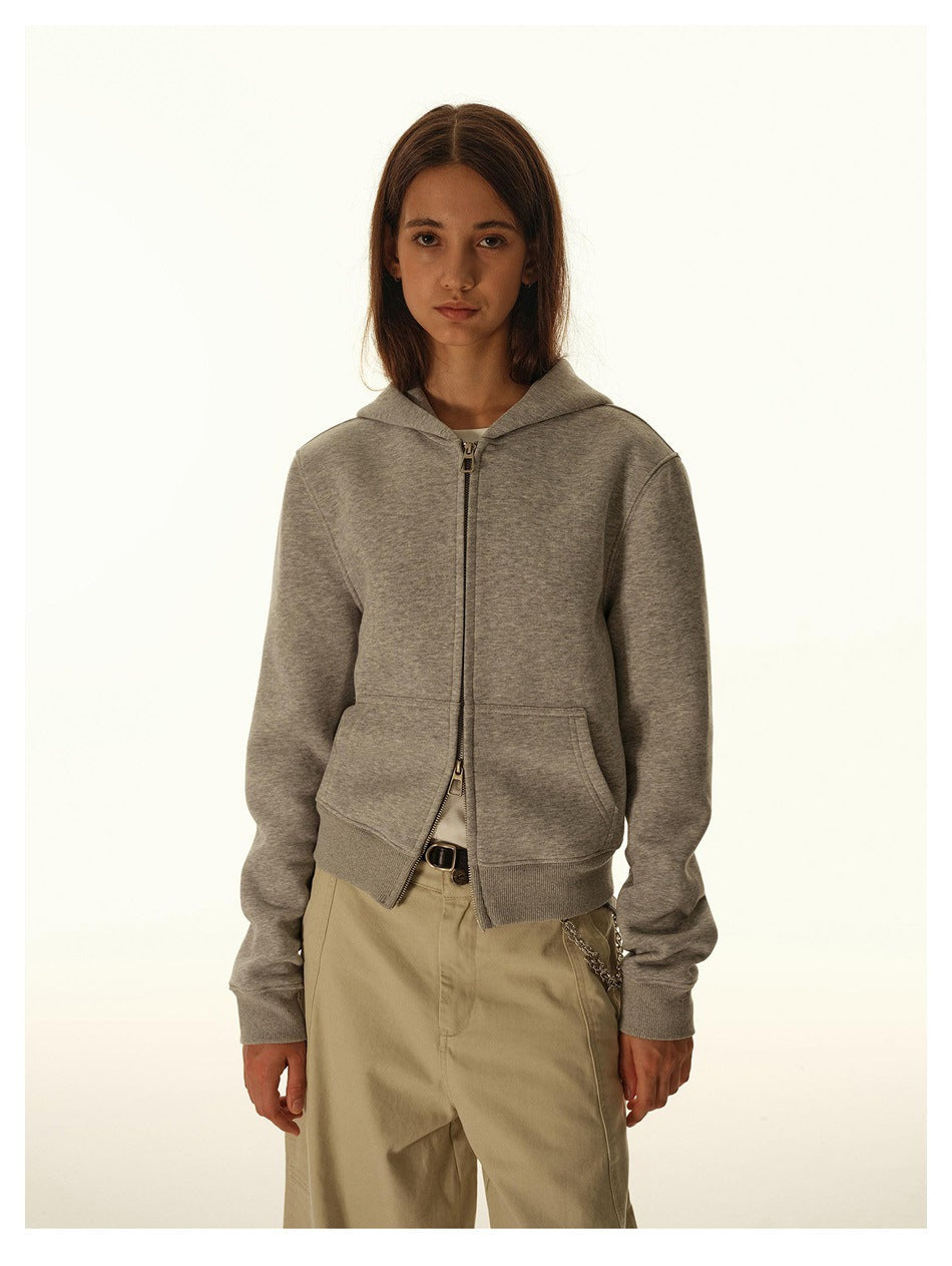 Woman wearing a light gray cropped zip-up hoodie with beige wide-leg pants, front view