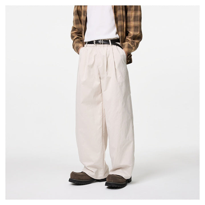 Person wearing off-white wide-leg pleated trousers with a plaid shirt, black belt and brown shoes, front view