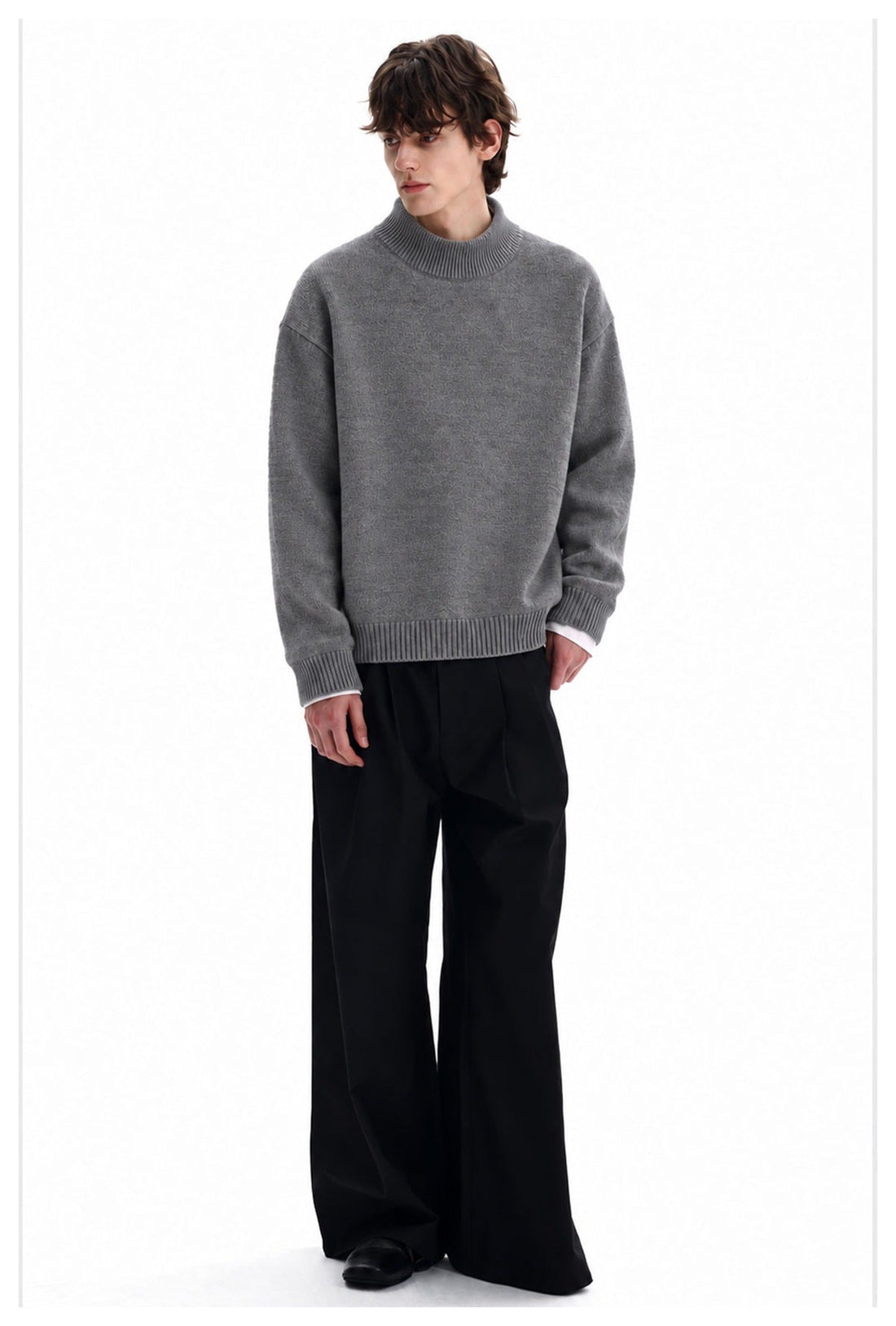 Full-length view of a man wearing a gray high-neck sweater with black wide-leg trousers.