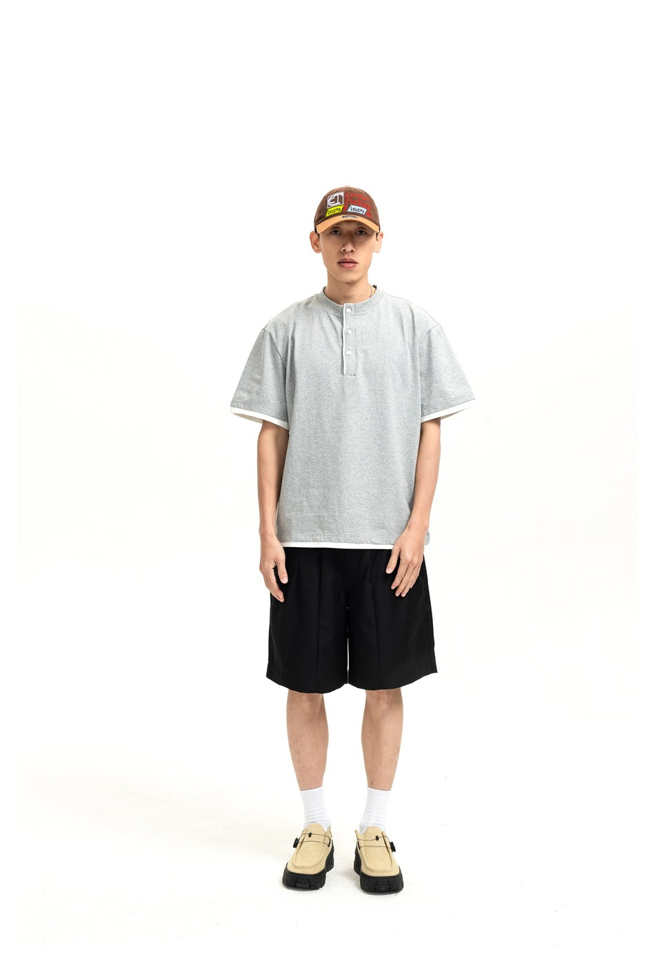 Man wearing a heather gray Henley T-shirt with white trim, black shorts, a cap and sneakers, front view