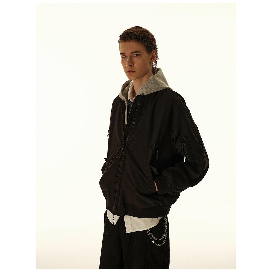 Man wearing a black zip-front bomber jacket over a gray hoodie, shown from an angled front view.
