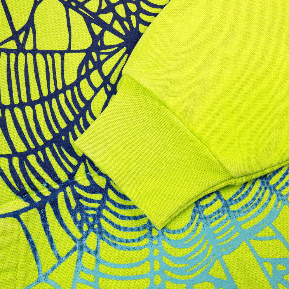 Close-up of a yellow sleeve resting on patterned fabric with blue and black web-like designs, evoking the style of the Sp5der Web Graphic Hoodie – Neon Green 440GSM Heavyweight Streetwear.