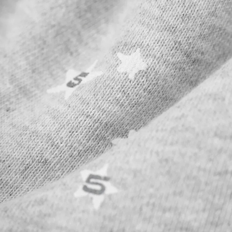 Close-up of light gray textured fabric from the Sp5der Atlanta Web Zip Hoodie – Grey 440GSM Heavyweight Streetwear, featuring printed white stars and a black number 5, showcasing bold streetwear details.