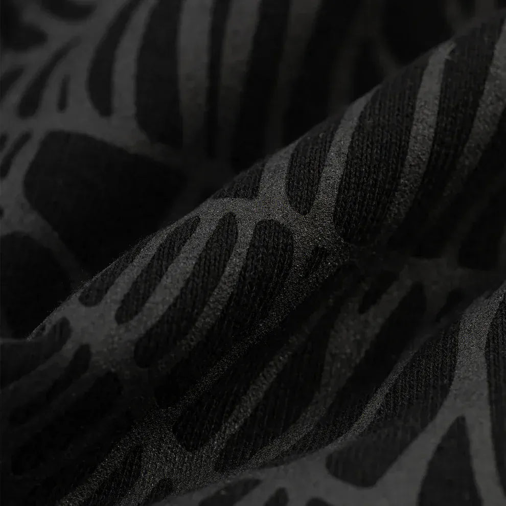 Close-up of black fabric from the Sp5der Tonal Web Zip Hoodie – Black 440GSM Heavyweight Streetwear, showcasing a raised abstract pattern and emphasizing the texture and folds of this premium zip hoodie.