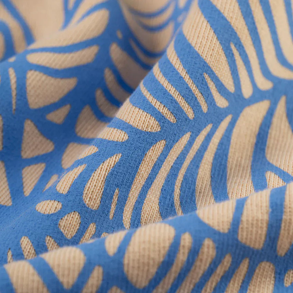 Close-up of the Sp5der “Sky Web” Hoodie—Cream/Blue/Green, 440GSM heavyweight cotton fleece with blue abstract line patterns; the oversized streetwear pullover fabric appears textured and slightly wrinkled.