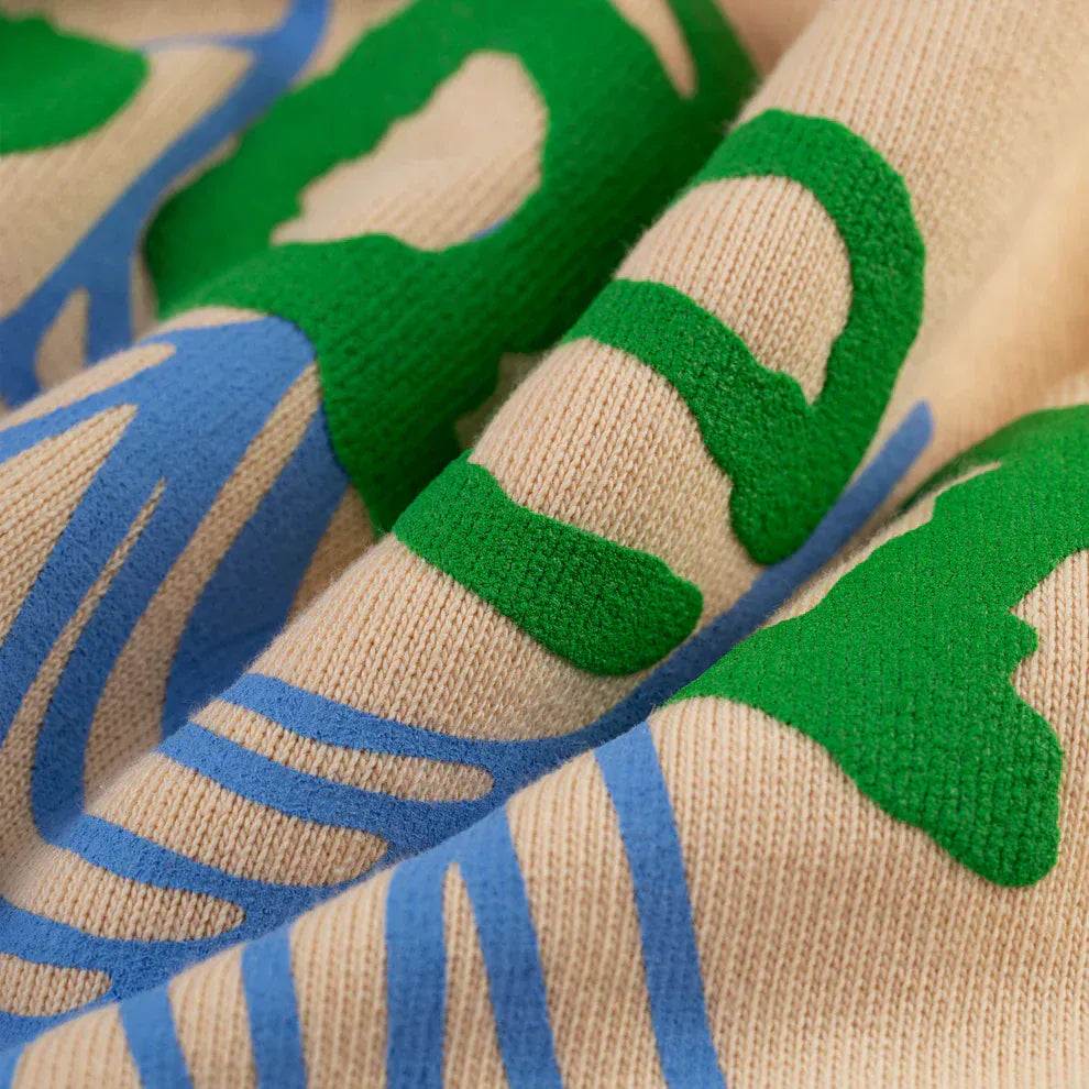 Close-up of the Sp5der “Sky Web” Hoodie—an oversized streetwear pullover in cream, blue, and green heavyweight 440GSM cotton fleece with abstract Y2K-inspired patterns.