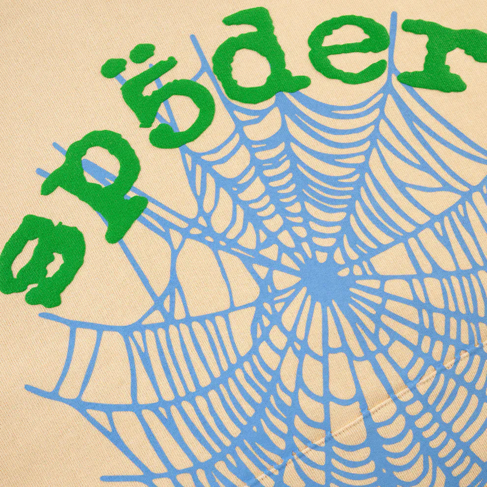 A blue spider web and green "sp5der" graphic stand out on a beige Sp5der “Sky Web” Hoodie—Cream/Blue/Green 440GSM Oversized Pullover—crafted from heavyweight cotton fleece, inspired by Y2K streetwear.