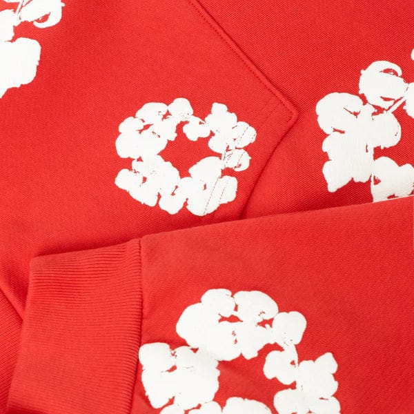 Close-up of the Red “Cotton Wreath” Denim Tears Hoodie, featuring red fabric with white floral prints and visible stitching, echoing the unique streetwear style of this pullover.