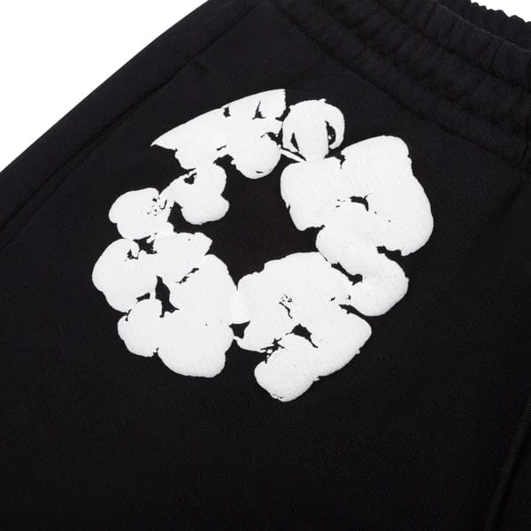 The Black “Cotton Wreath” Denim Tears Sweatpants feature an elastic waistband and a white floral print inspired by the iconic streetwear style.