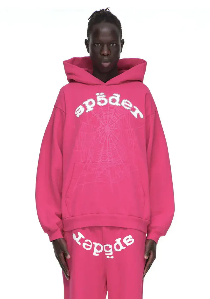 A person wears the Sp5der Web Hoodie – Hot Pink 440GSM Heavyweight Streetwear Pullover and matching pants, both in streetwear style featuring "sp5der" and a bold white spider web graphic on the hoodie.