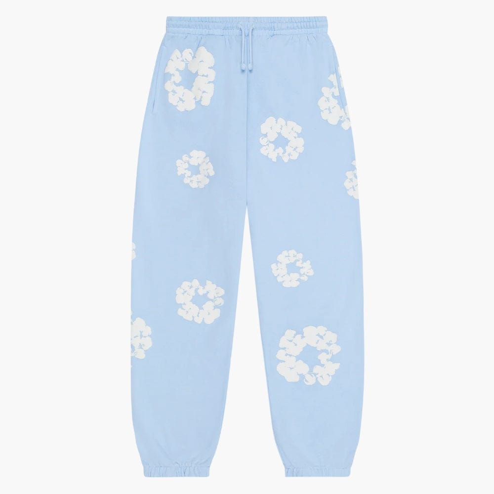 The Light Blue “Cotton Wreath” Denim Tears Sweatpants feature an elastic waistband and cuffs, and are adorned with white floral prints for a fresh, modern streetwear vibe.
