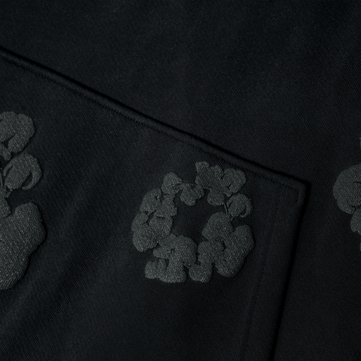 A close-up of the Black Monochrome “Cotton Wreath” Denim Tears Hoodie shows its raised floral pattern, a subtle textured detail ideal for streetwear fans or anyone seeking the hoodie’s signature cotton wreath motif.