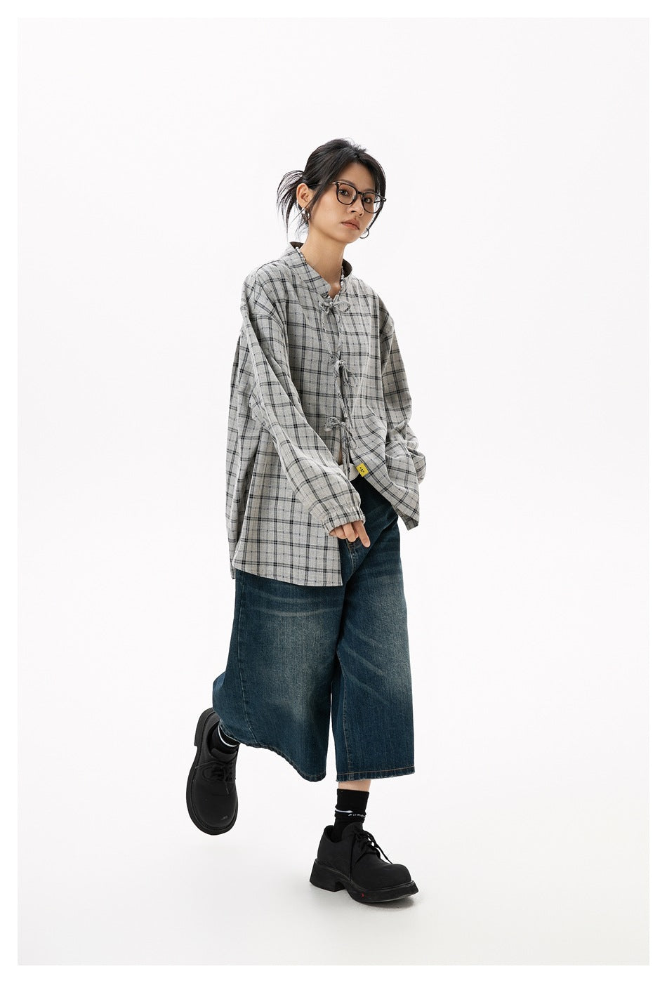 Model posing in an oversized gray plaid tie-front shirt with cropped blue jeans and black shoes