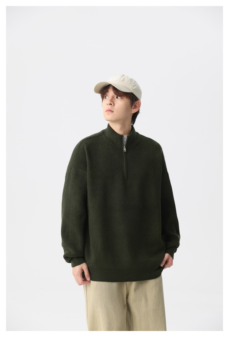 Model wearing a dark olive ribbed quarter-zip sweater with beige trousers, shown from the front.