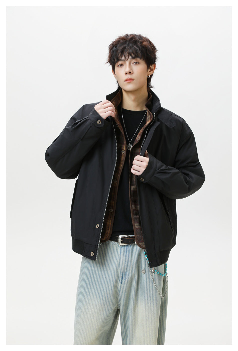 Model wearing black stand-collar jacket open over a plaid layer, black tee and striped light-wash pants