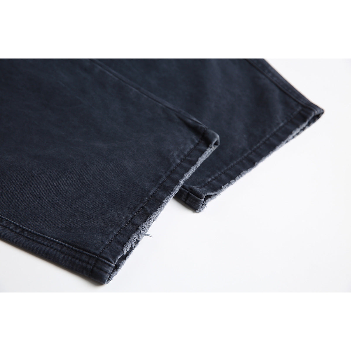 Close-up of dark navy pant legs showing stitched seams and unfinished, slightly frayed hems.