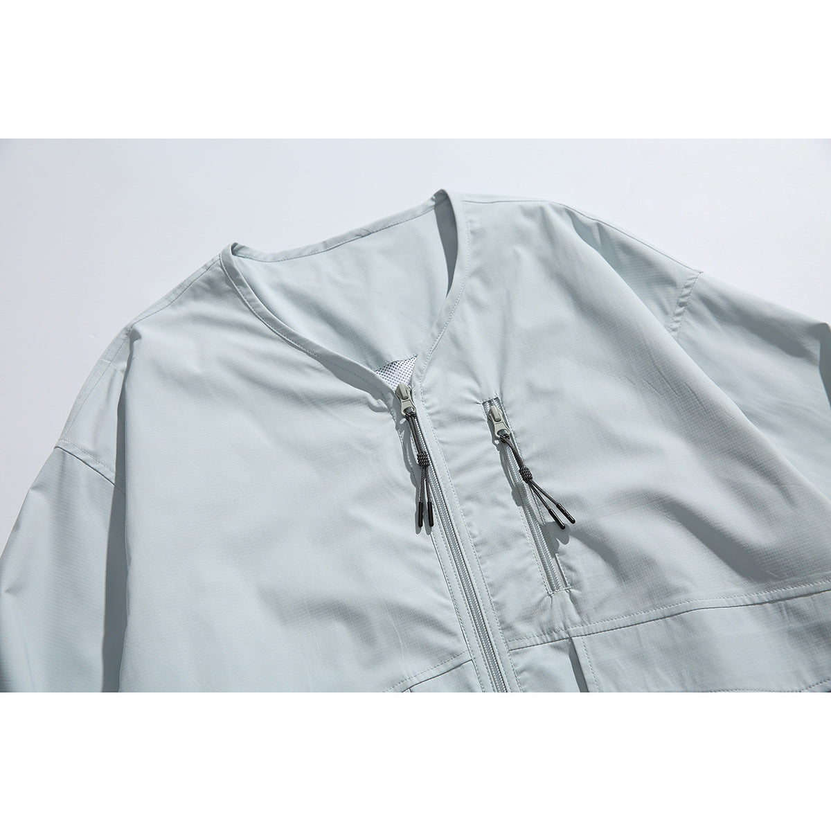 Close-up of a pale blue jacket front with a V-neck, central zipper, and vertical zip chest pocket.