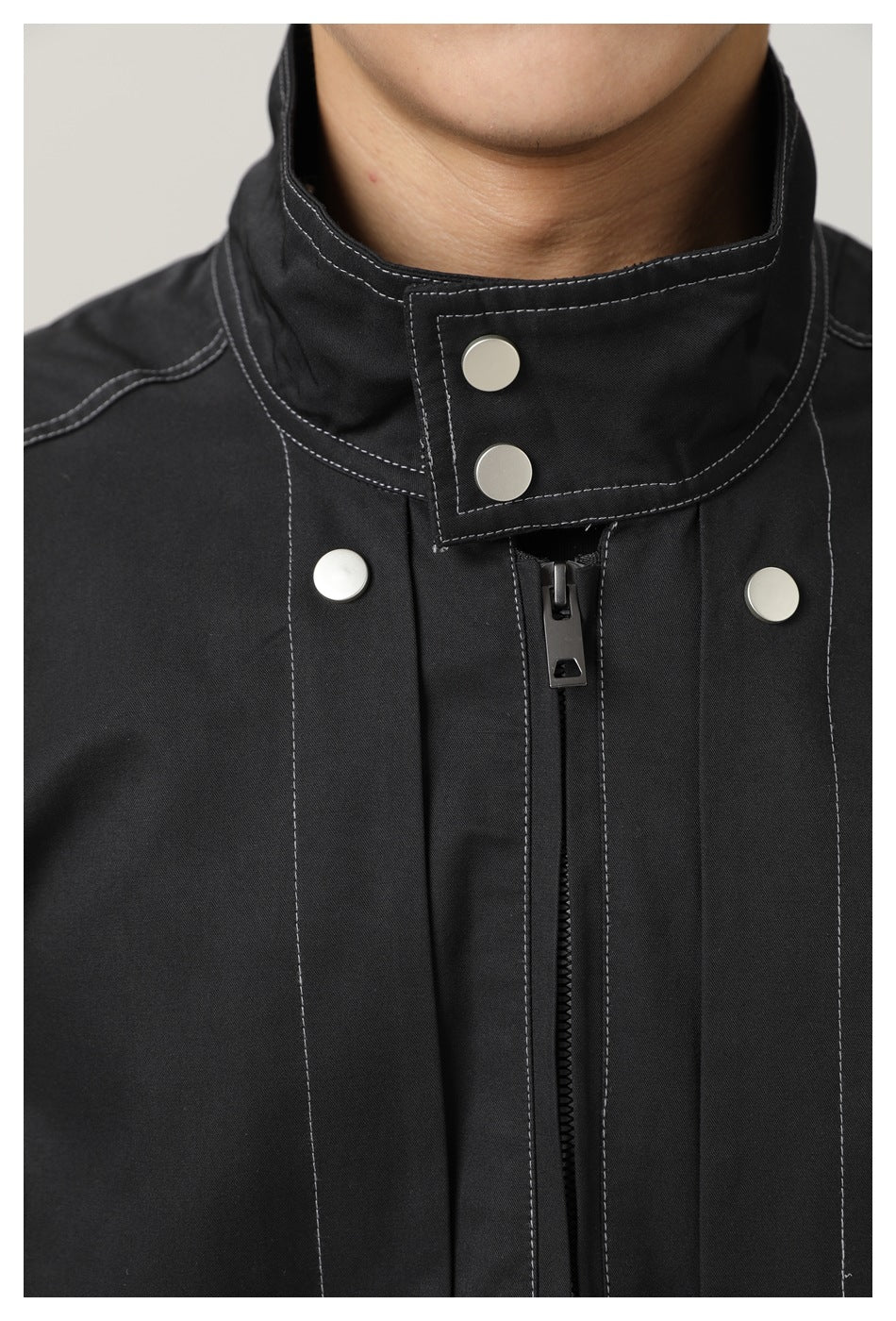 Close-up of the black jacket's stand collar, contrast stitching, silver snaps and central zipper.