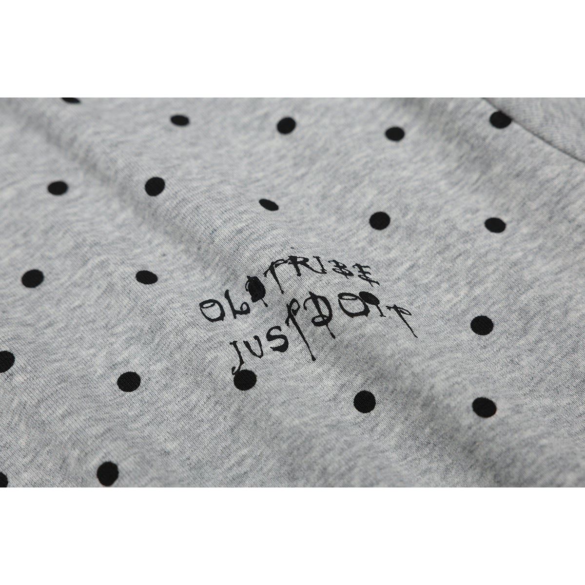Close-up of black polka dots and stylized black lettering printed on gray heather polo fabric.