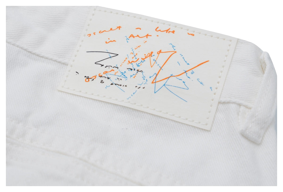Close-up of a white garment with a stitched rectangular patch featuring orange, blue, and black abstract markings.