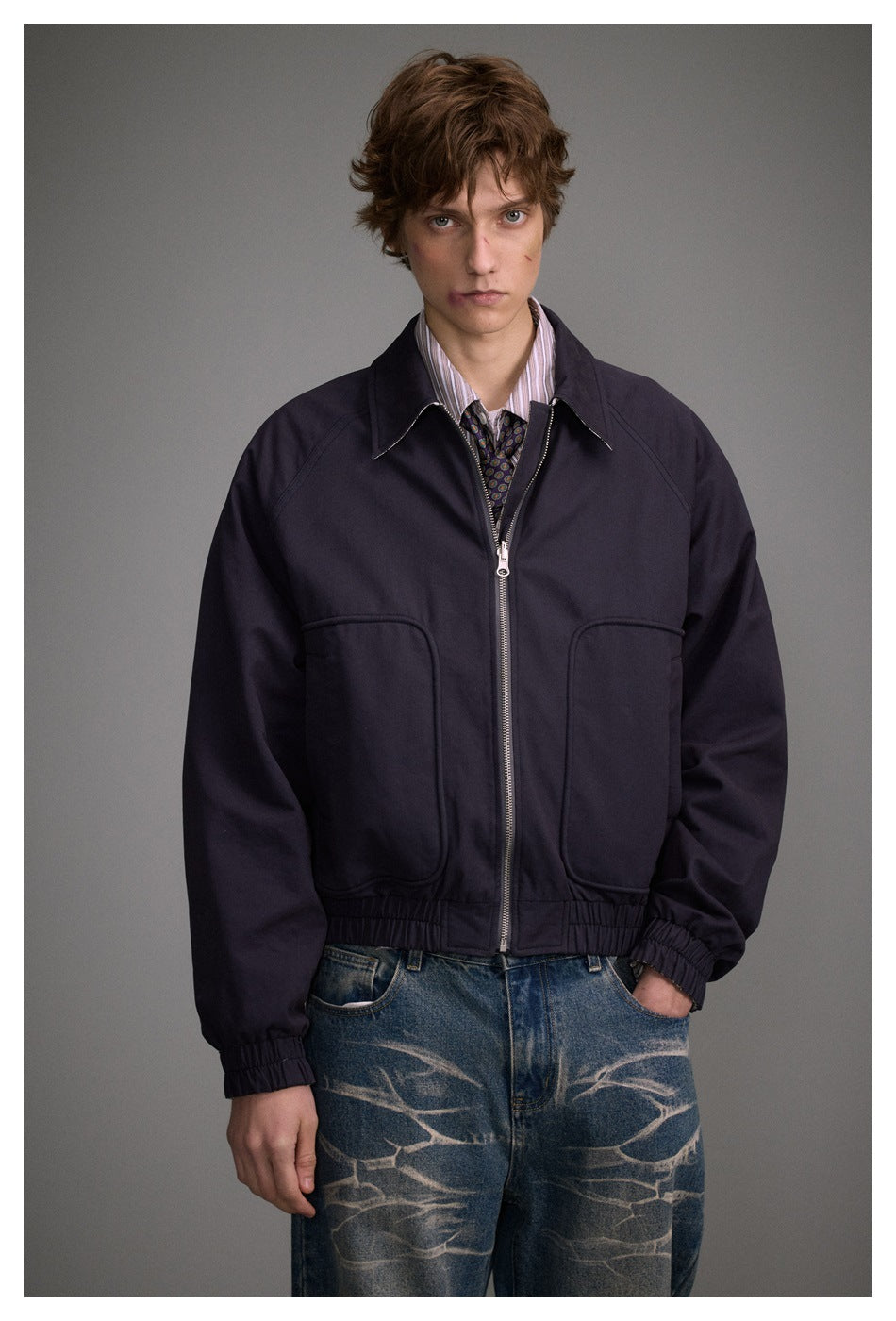 Front view of a model wearing a dark navy jacket with a silver zipper, pointed collar, large pockets and elastic cuffs.