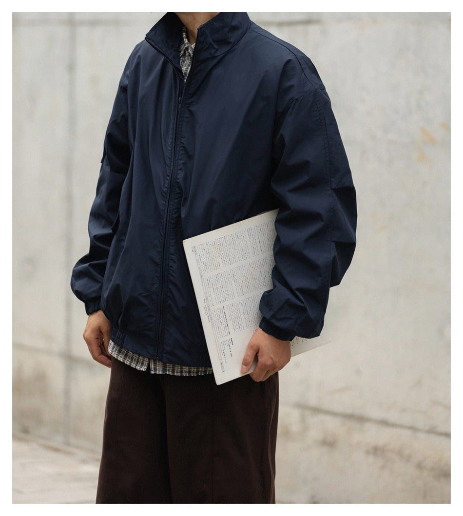 Torso view of a person wearing a navy zip jacket over a plaid shirt, holding a magazine against a concrete wall