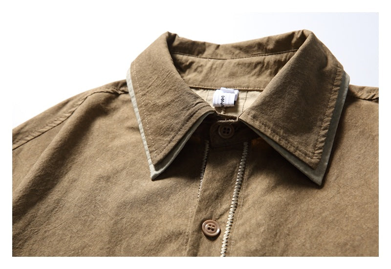 Close-up of a brown shirt collar with pale edge trim, a button, and a small neck label.