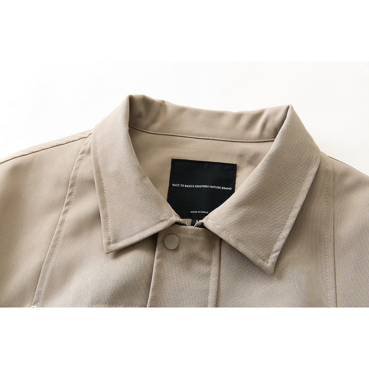 Close-up of a beige jacket collar, snap, and interior label with English text.