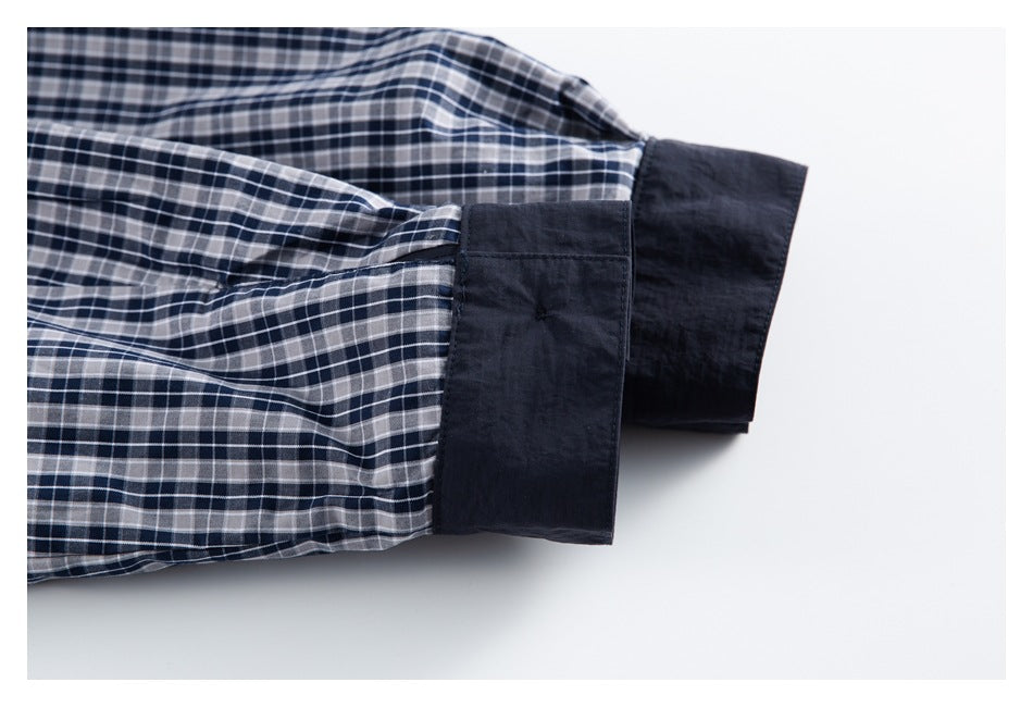 Close-up of a navy, gray, and white plaid shirt sleeve with a solid navy cuff.