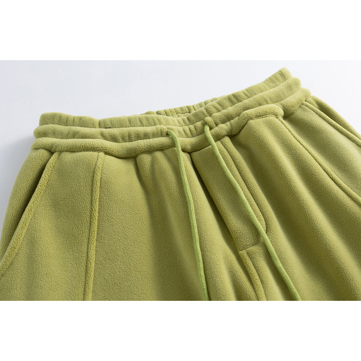 Close-up of olive green pants showing the elastic waistband, drawstring, seams, and side pocket opening.