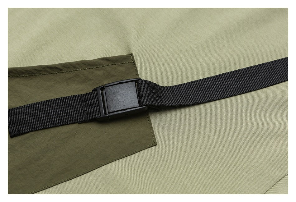 Close-up of a black webbing strap and buckle over an olive-green garment pocket.