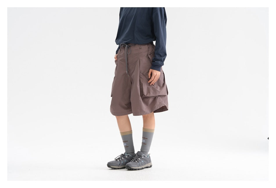 Person wearing dusty purple wide-leg shorts with a navy top and gray sneakers, angled side view