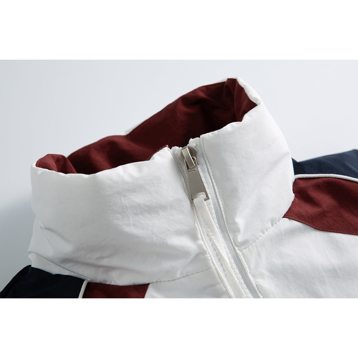 Close-up of a white jacket’s tall collar, burgundy lining and large front zipper, with navy and burgundy panels visible.