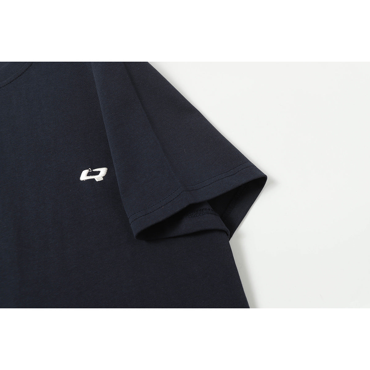 Close-up of a navy T-shirt sleeve and chest with a small white embroidered emblem.