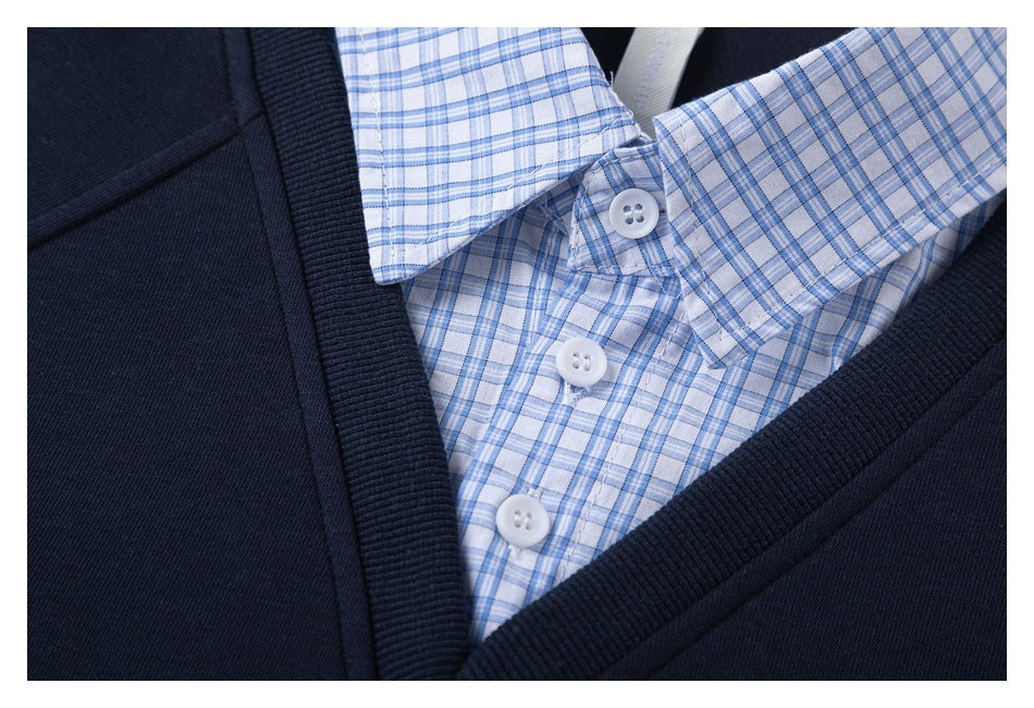 Close-up of the blue checked shirt collar and white buttons framed by the ribbed V-neck of a navy sweatshirt.
