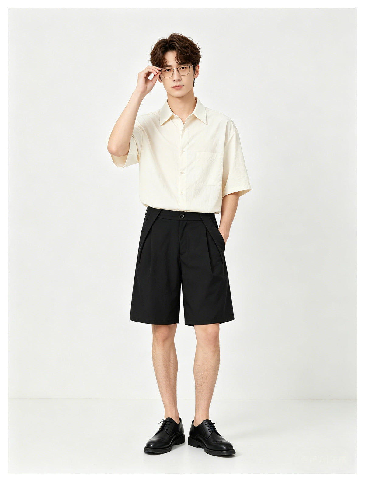 Model wearing an ivory short-sleeve button-up shirt and black pleated shorts, front view.