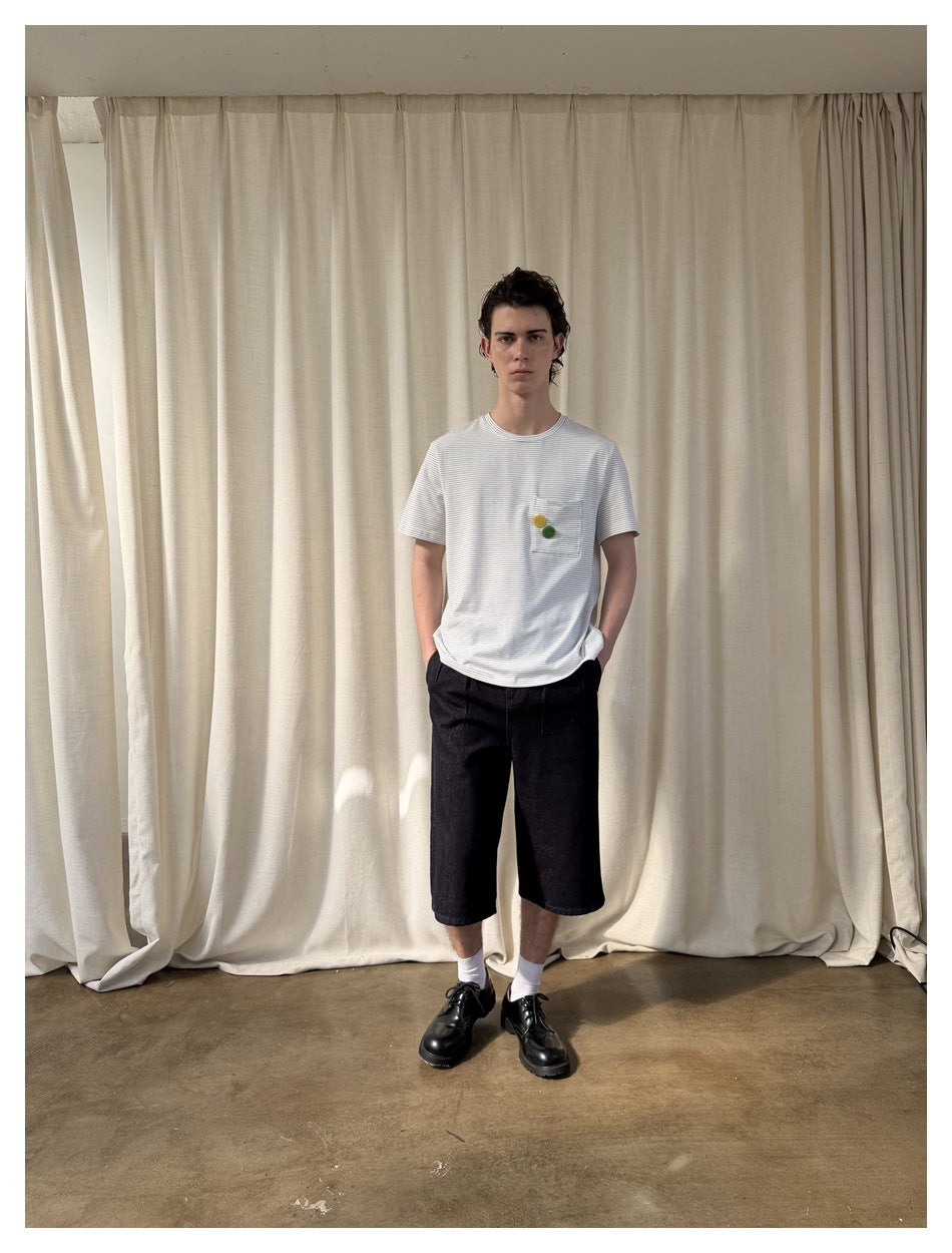 Full-length view of a model wearing a white fine-blue-striped pocket T-shirt, black shorts, white socks, and black shoes.