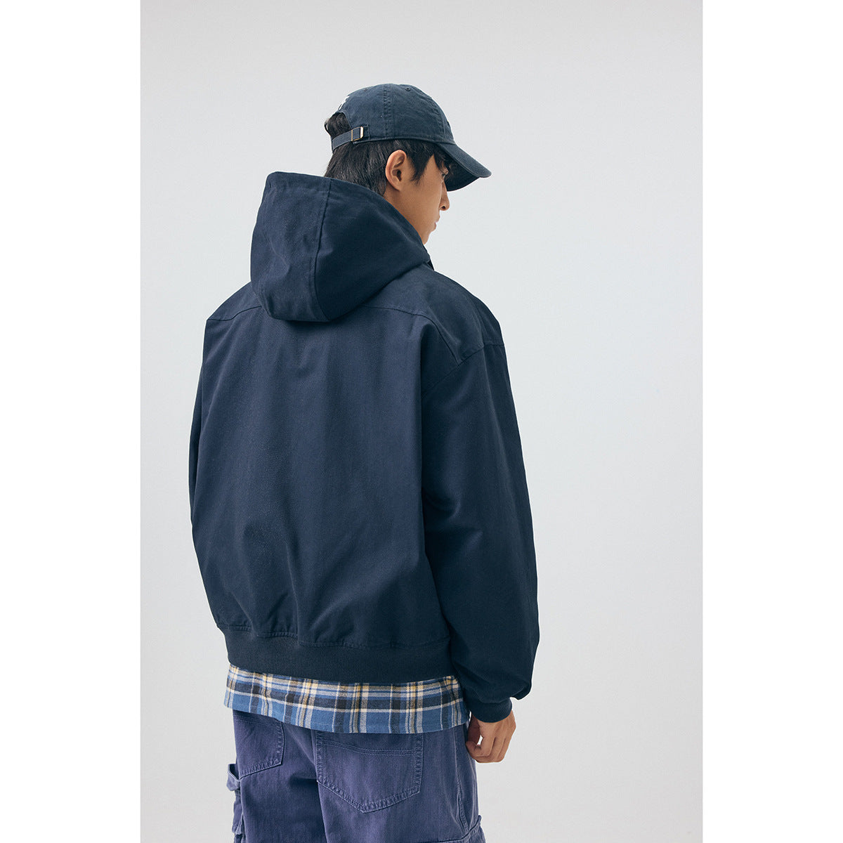 Back view of a model wearing a navy hooded jacket, with a blue plaid shirt visible below the hem.
