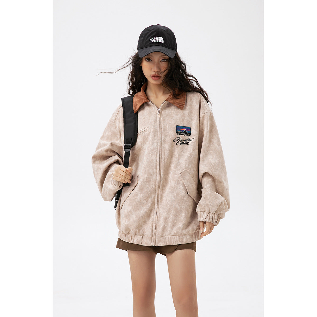 Model wearing a light beige zip jacket with a brown collar, chest embroidery, and elastic cuffs.