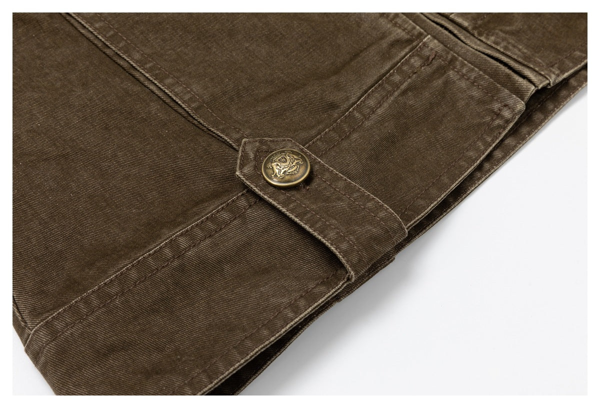 Brown garment hem detail with a stitched fastening tab and ornate brass-tone button.