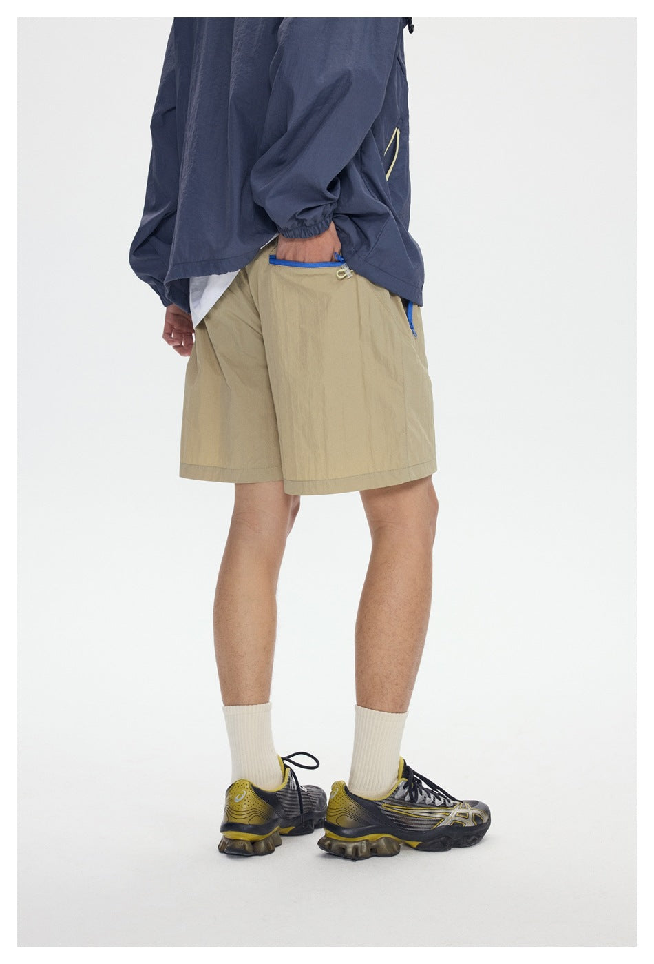 Side view of a model wearing khaki shorts with bright blue pocket zippers and a navy jacket.