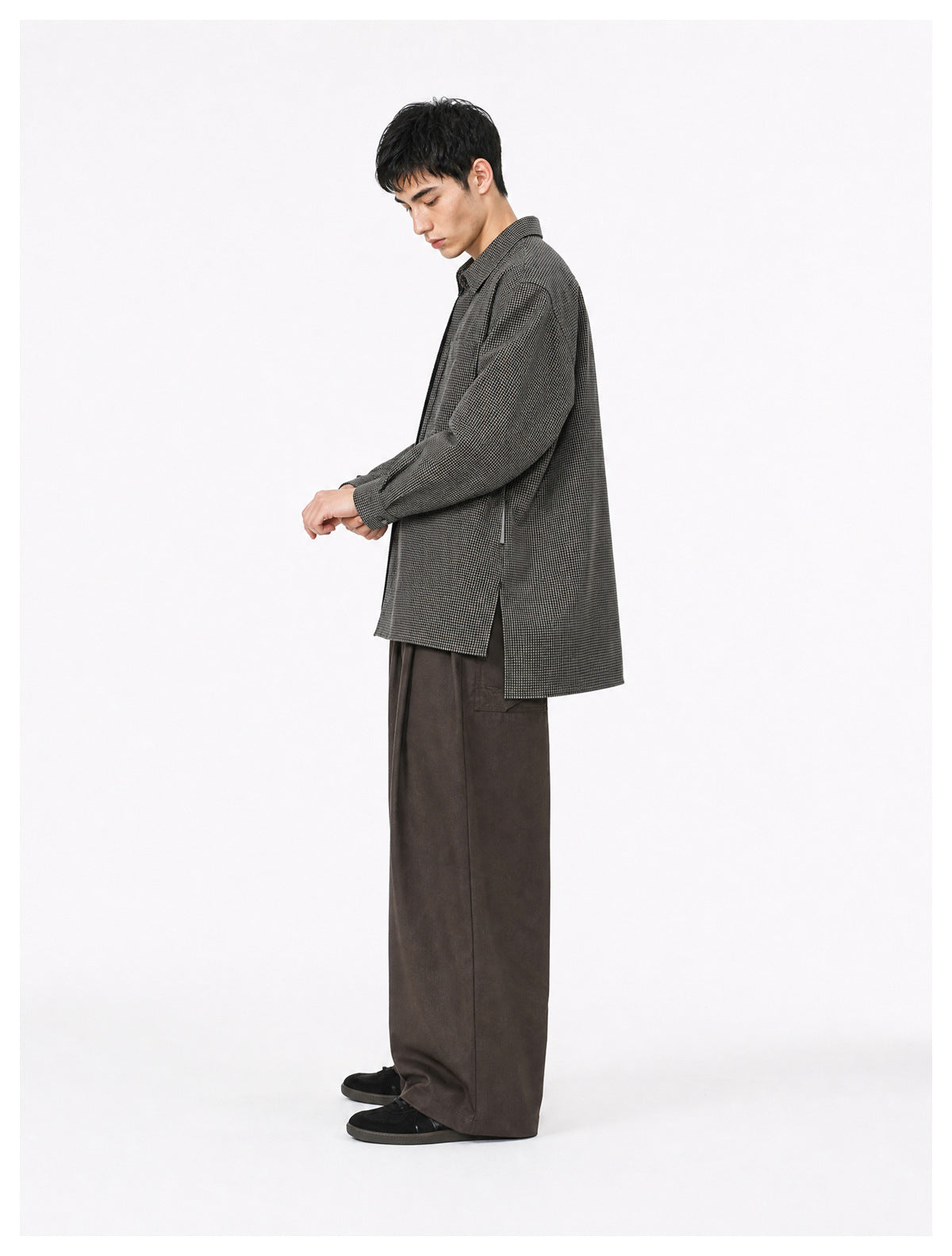 Side view of a model wearing a black check shirt jacket with side slit over wide brown pants