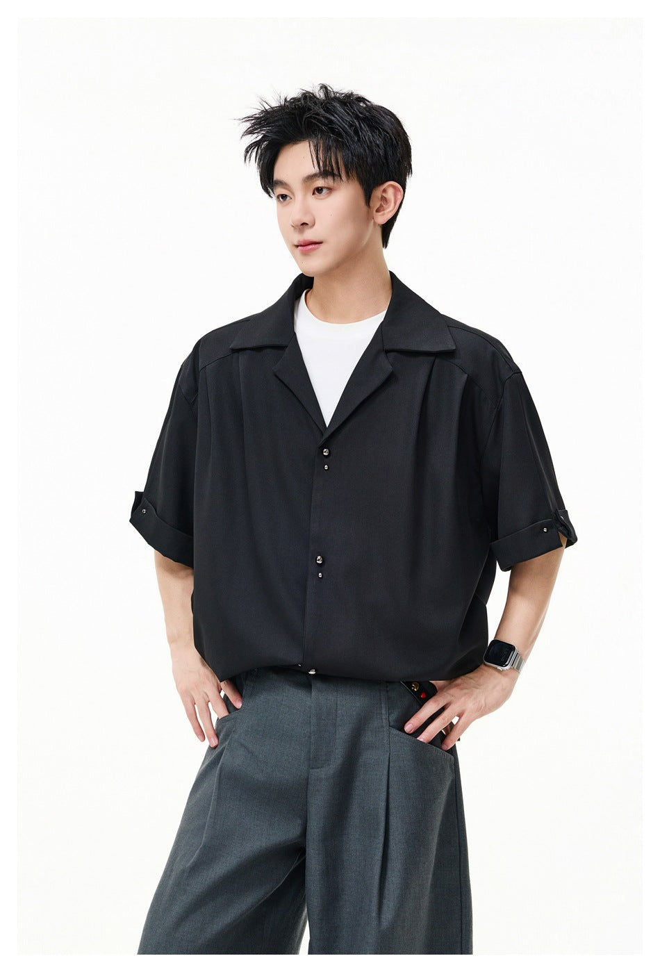 Man wearing black short-sleeve shirt with stud buttons over a white tee and gray pleated trousers