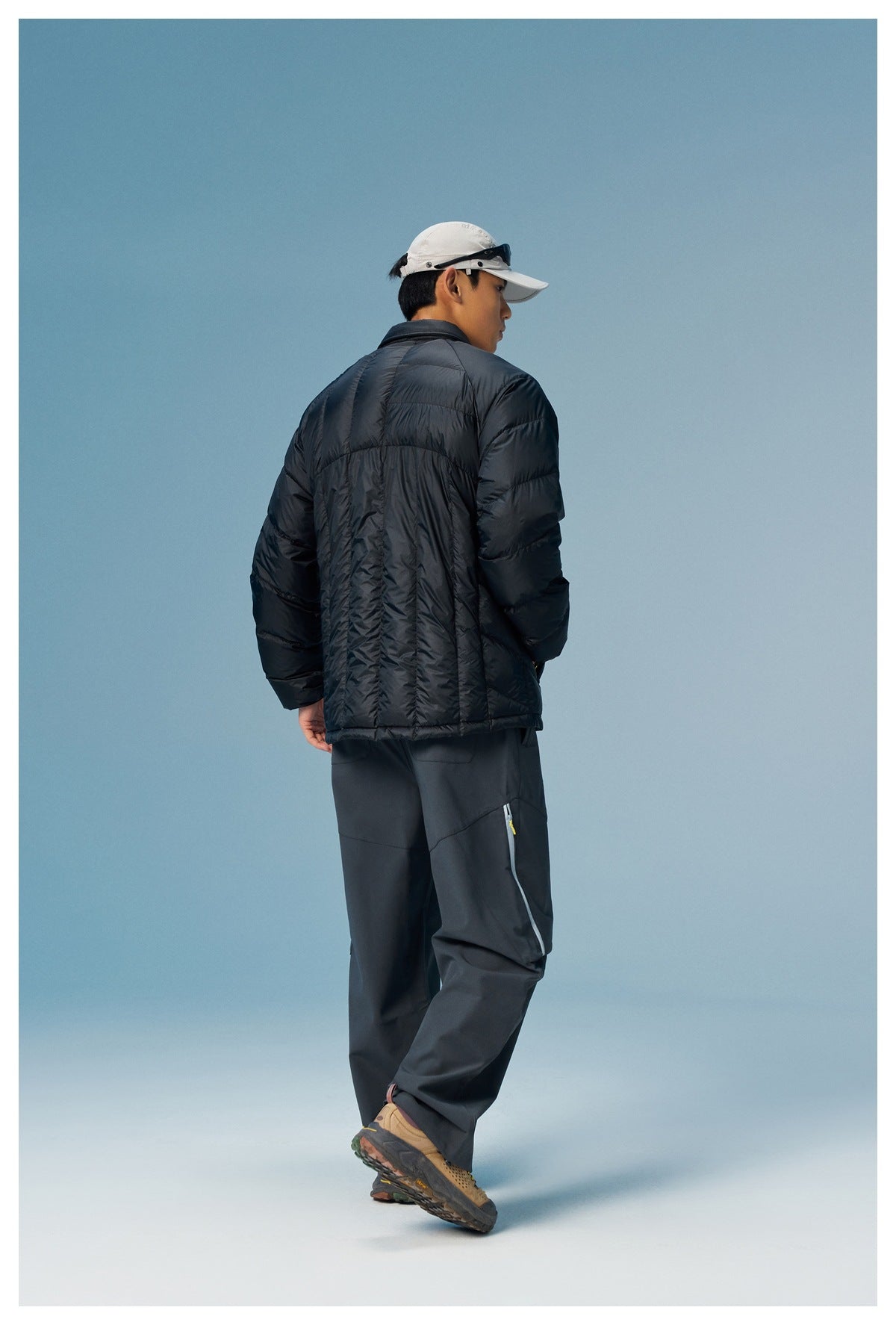 Rear view of a model wearing a black quilted puffer jacket with dark trousers.
