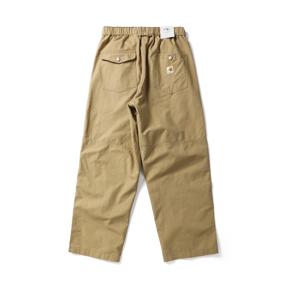 Rear view of loose tan trousers with an elastic waistband and two snap-flap back pockets.