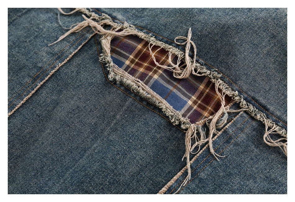 Close-up of a frayed opening in blue denim revealing brown, blue, and cream plaid fabric beneath.