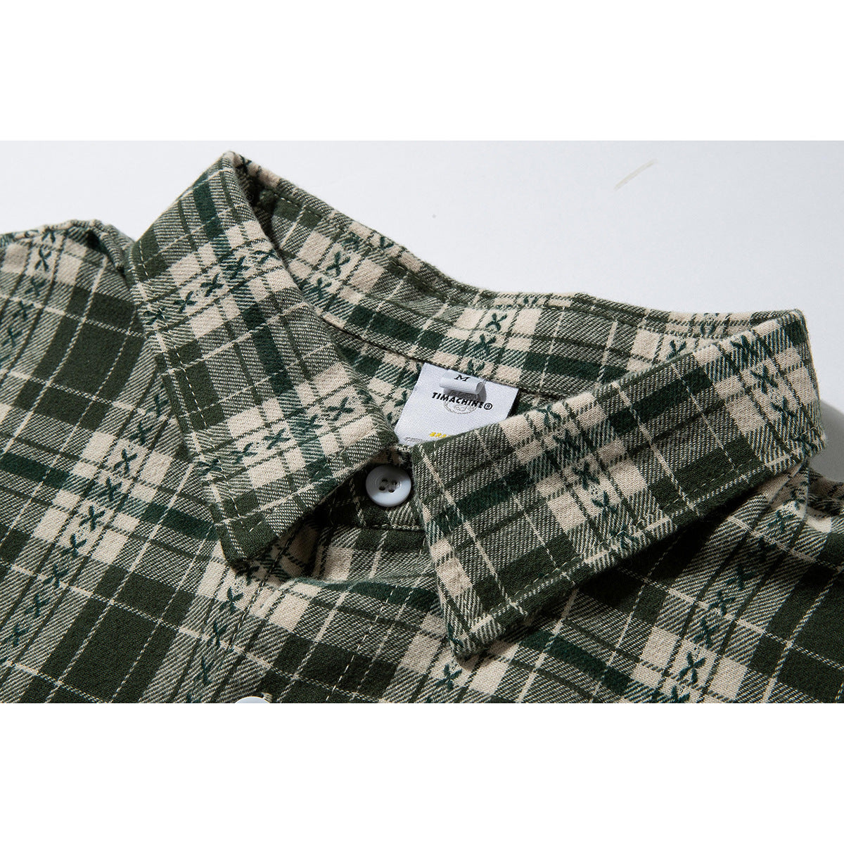 Close-up of a pointed collar and top button on a dark green and cream plaid shirt.