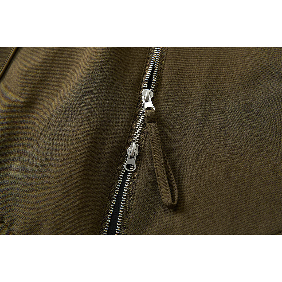 Close-up of the olive-brown jacket's silver double zipper pulls and stitched zipper placket.