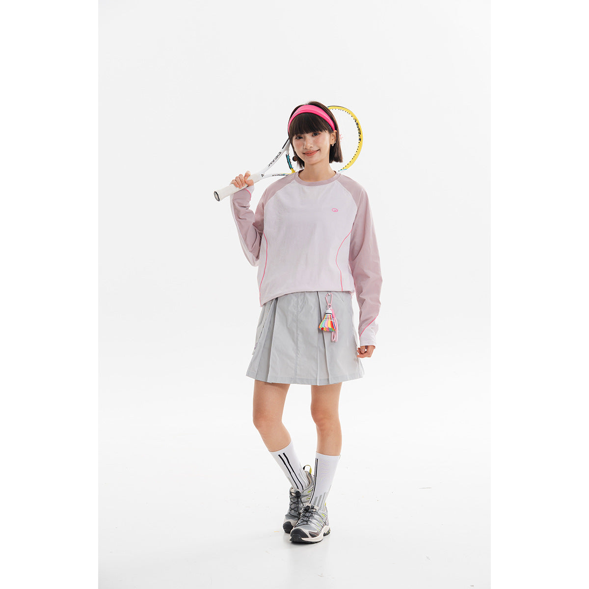 Model wearing a pale lavender long-sleeve top with pink piping and a light gray pleated tennis skirt.